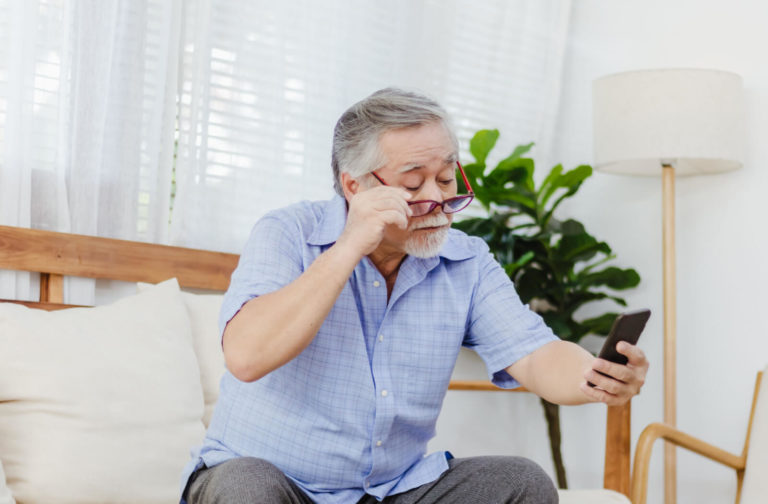 An older man lowering his glasses and squinting at a smartphone.